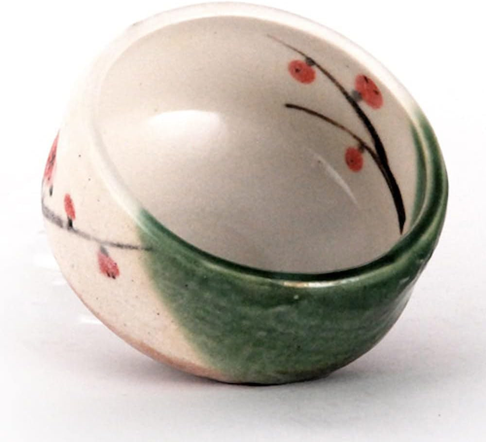 The bowl tilted to show the inside, a plum branch painted across the white glaze and green glaze down the outer wall