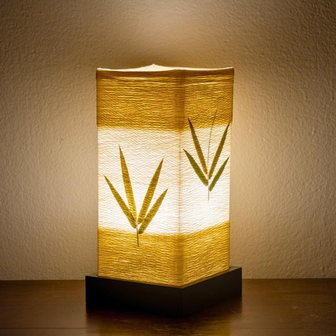 The lantern lit against a pale wall, two sprays of bamboo leaf showing through the paper