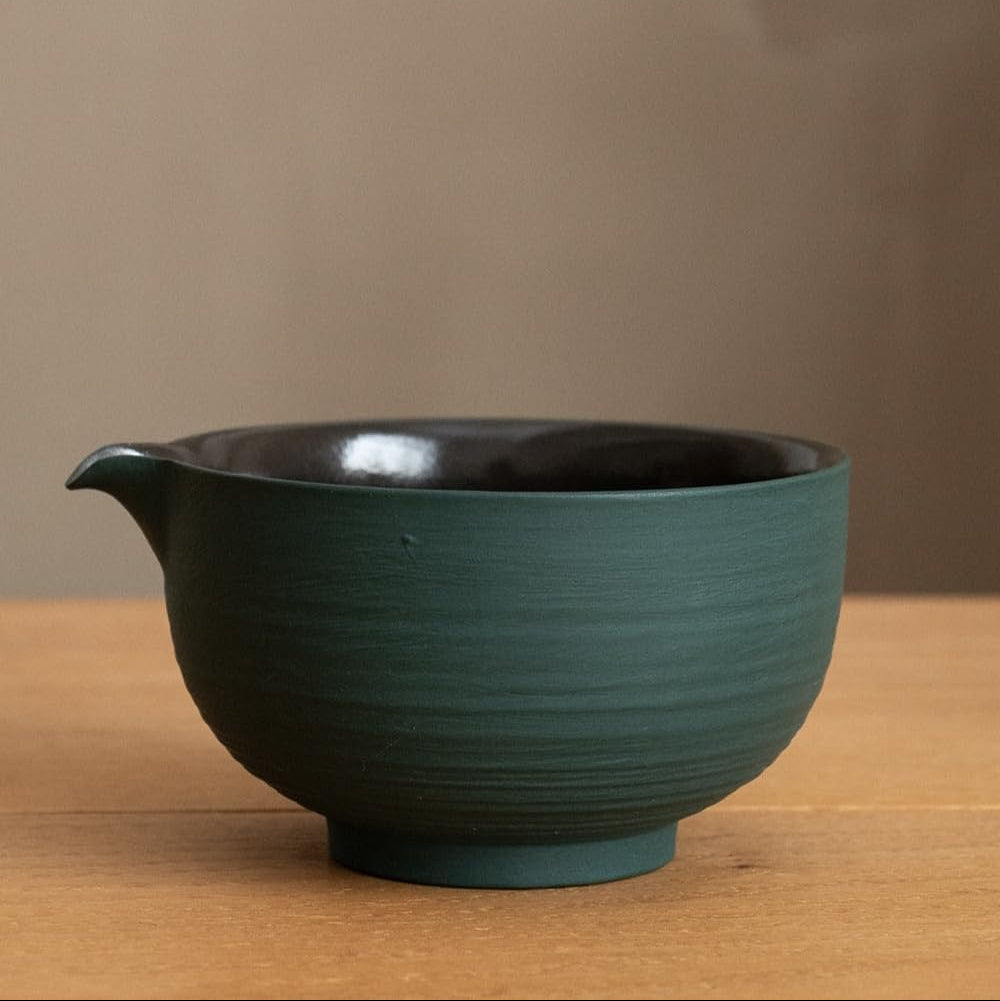 The green chawan seen from the side, showing the pouring spout and the dark glazed interior