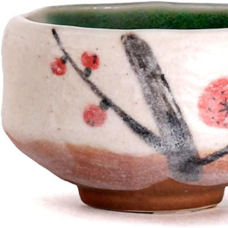 The bowl seen straight on against white, red plum blossoms on a black branch, green glaze inside the rim, bare clay at the base