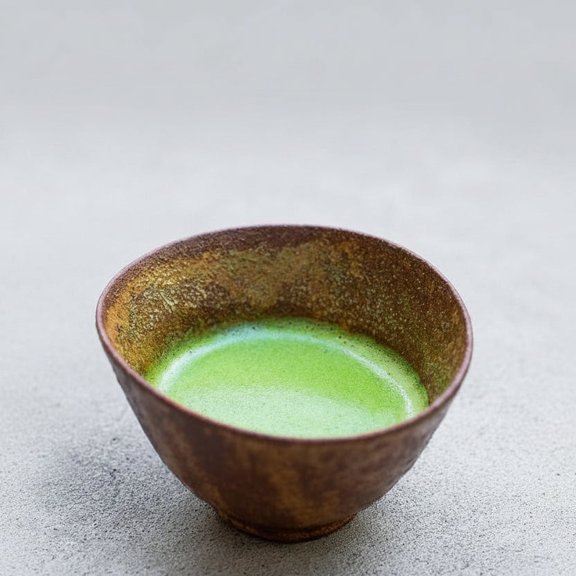 Matcha whisked in a bowl, a bamboo whisk beside it and a plate of wagashi behind