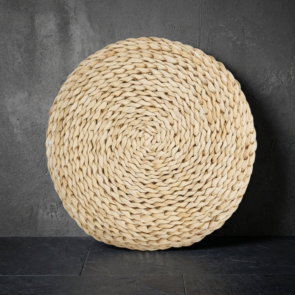 The round cushion stood on its edge against a grey concrete wall, showing the spiral of braided cattail