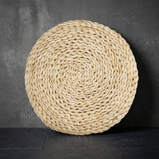 The round cushion stood on its edge against a grey concrete wall, showing the spiral of braided cattail