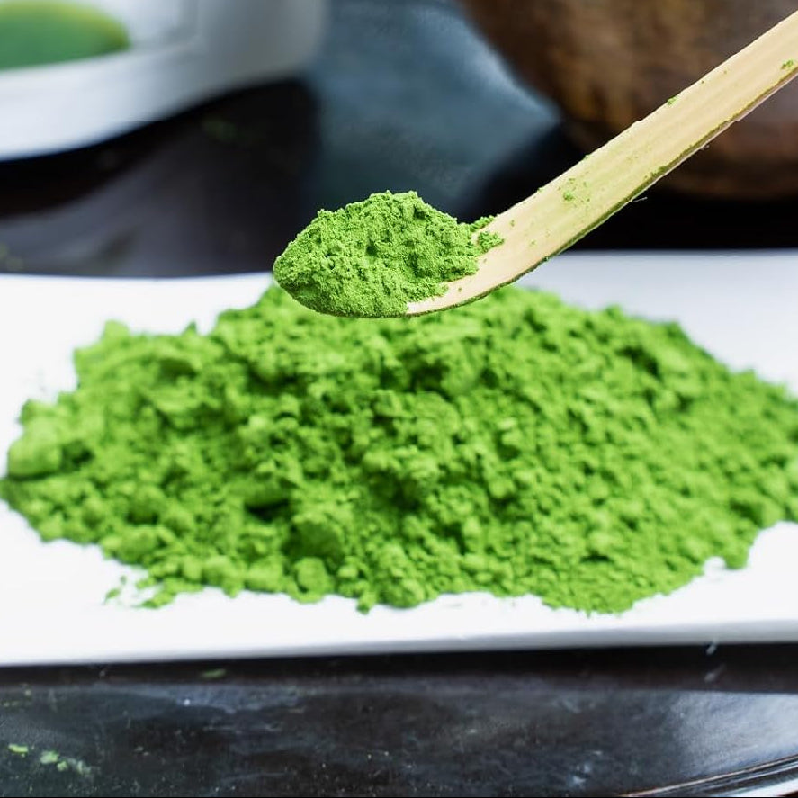 Bright green matcha powder on a bamboo scoop, above a mound of sifted powder